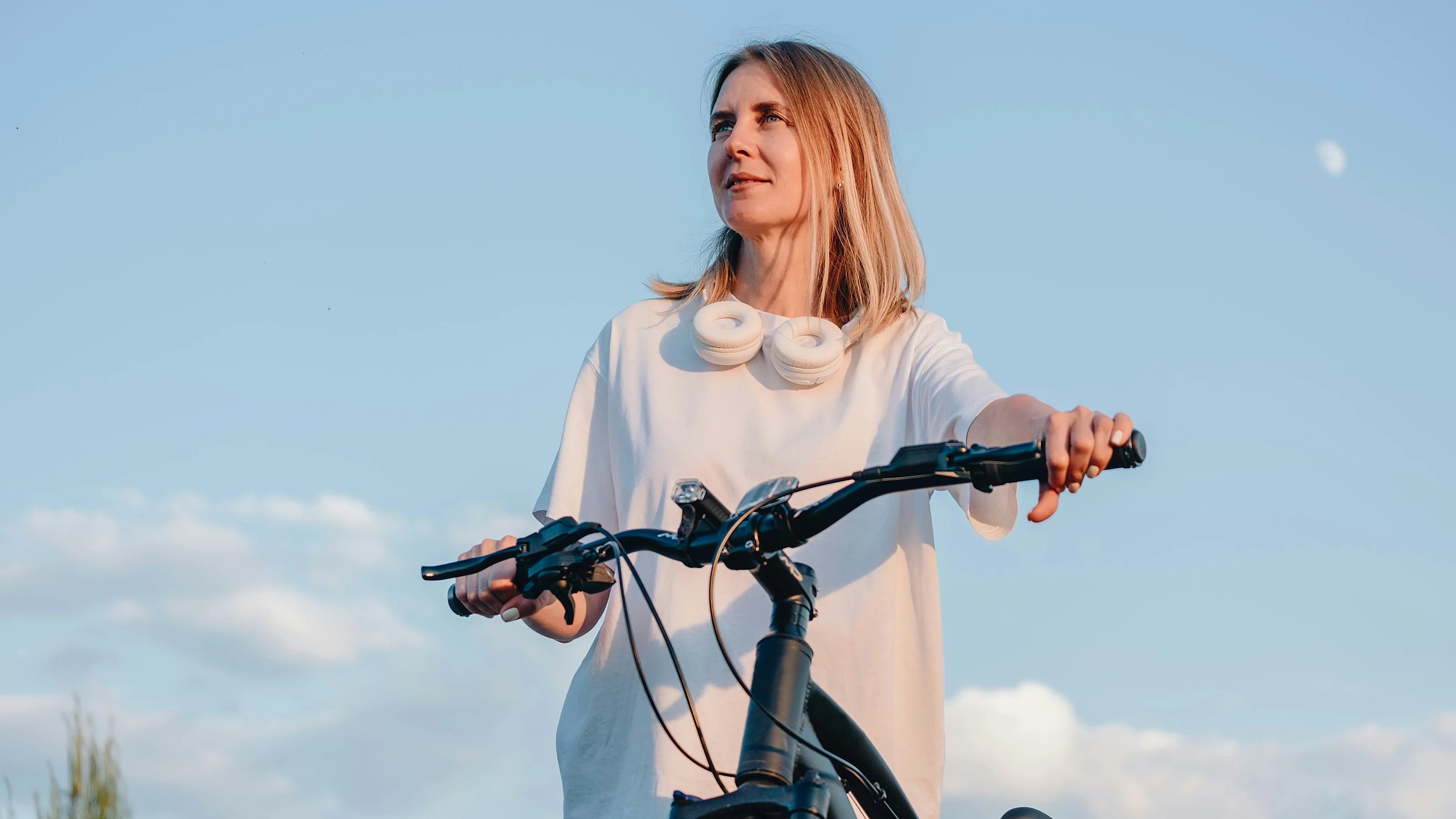 A woman with her bicycle against an open evening sky