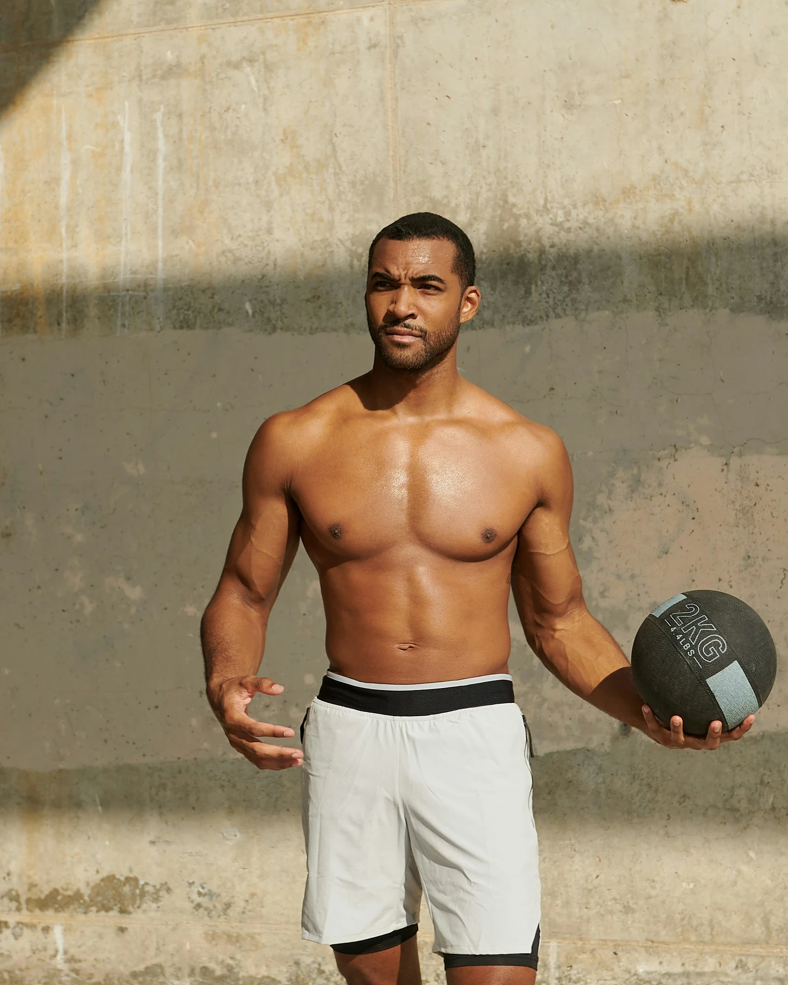A man training with a medicine ball against a sunlit wall