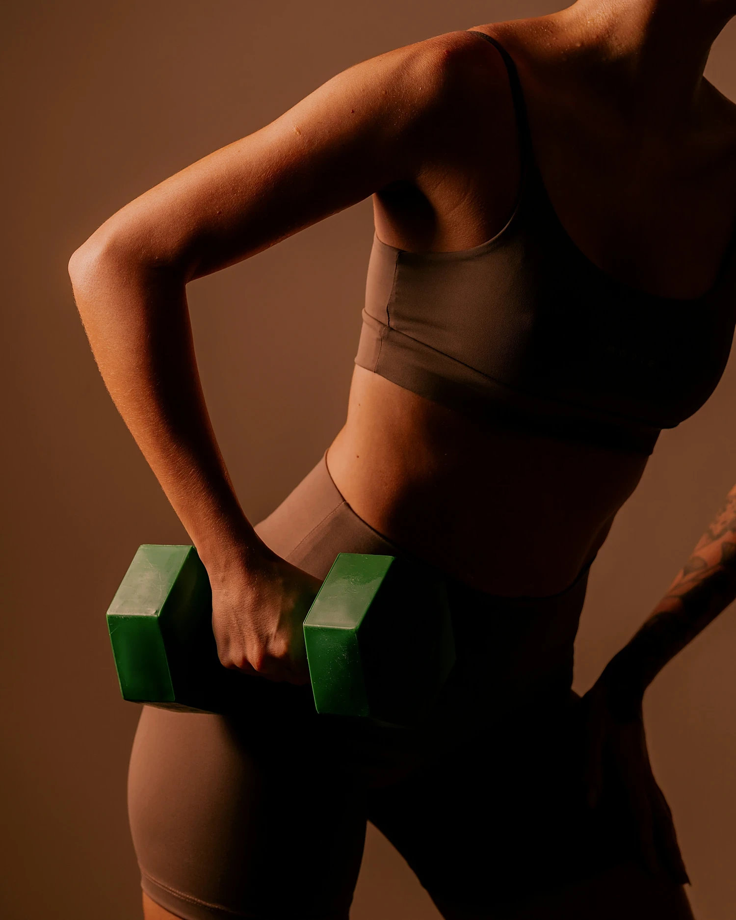 A woman holding a dumbbell in warm studio light