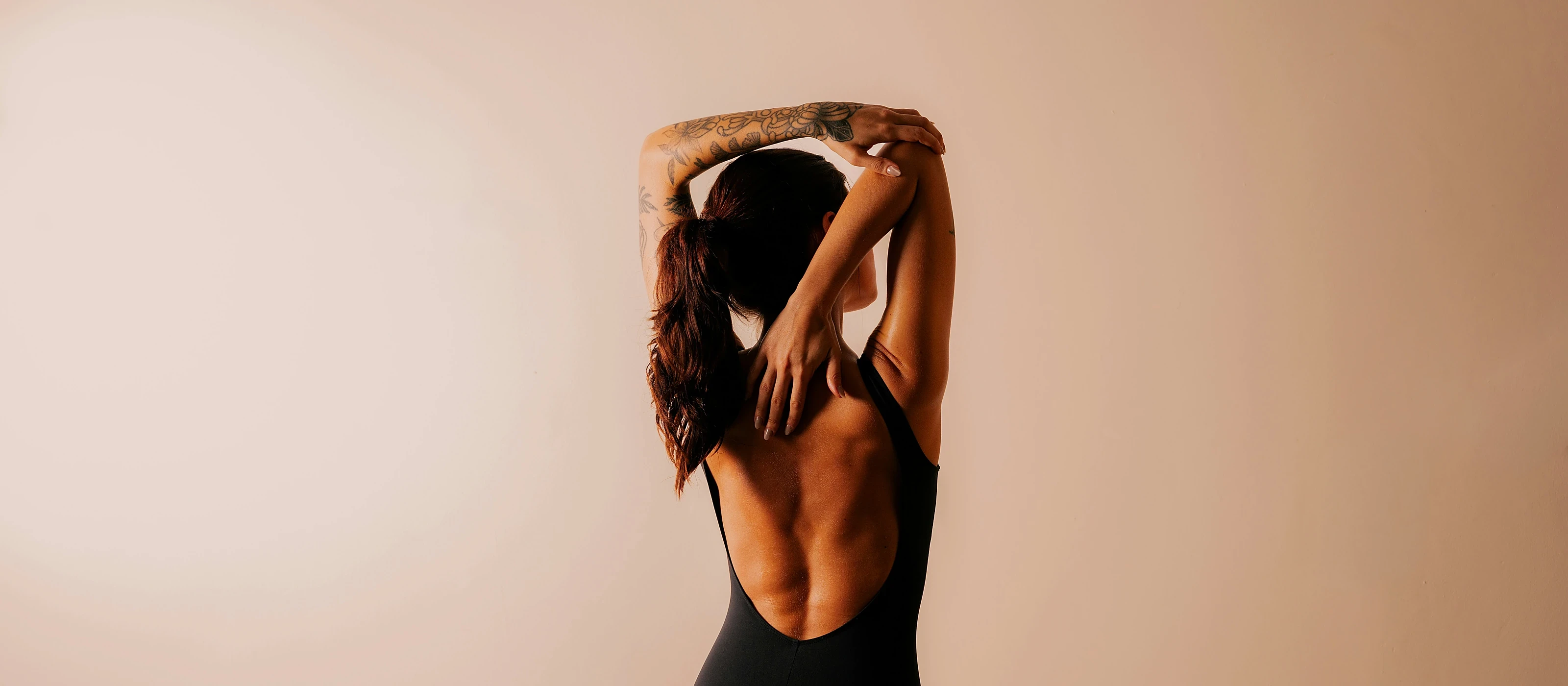 A woman stretching with arms overhead in studio light